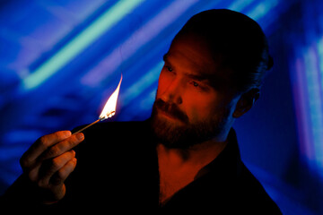 Bearded man looking at match flame against blue neon lighting