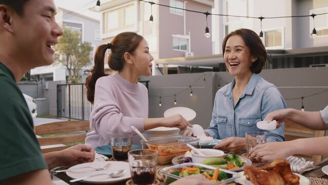 Love care giver Mother's day share serve scoop rice pass for middle age mum at home patio dine table party. Group of young asia people enjoy warm time eat thai picnic meal to adult parent mature mom.