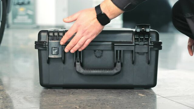 A mechanical engineer opens a box with working tools. Close-up of a worker's hand opening a black box.