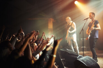 Shot of a crowd of music fans reaching up at a guitarist on stage. This concert was created for the...