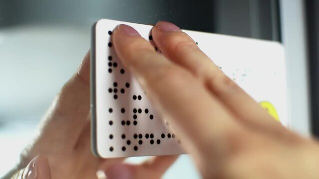Person with blindness touches and reads with his hands the Braille text plate on the door of a train or bus. Close-up of fingers touching relief of points in public transport. Sightless, low vision.