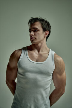 Strong hands. Sportsman. Handsome young man with muscular relief body posing in singlet over studio background. Concept of man's beauty, sportive and healthy lifestyle, fashion, stength