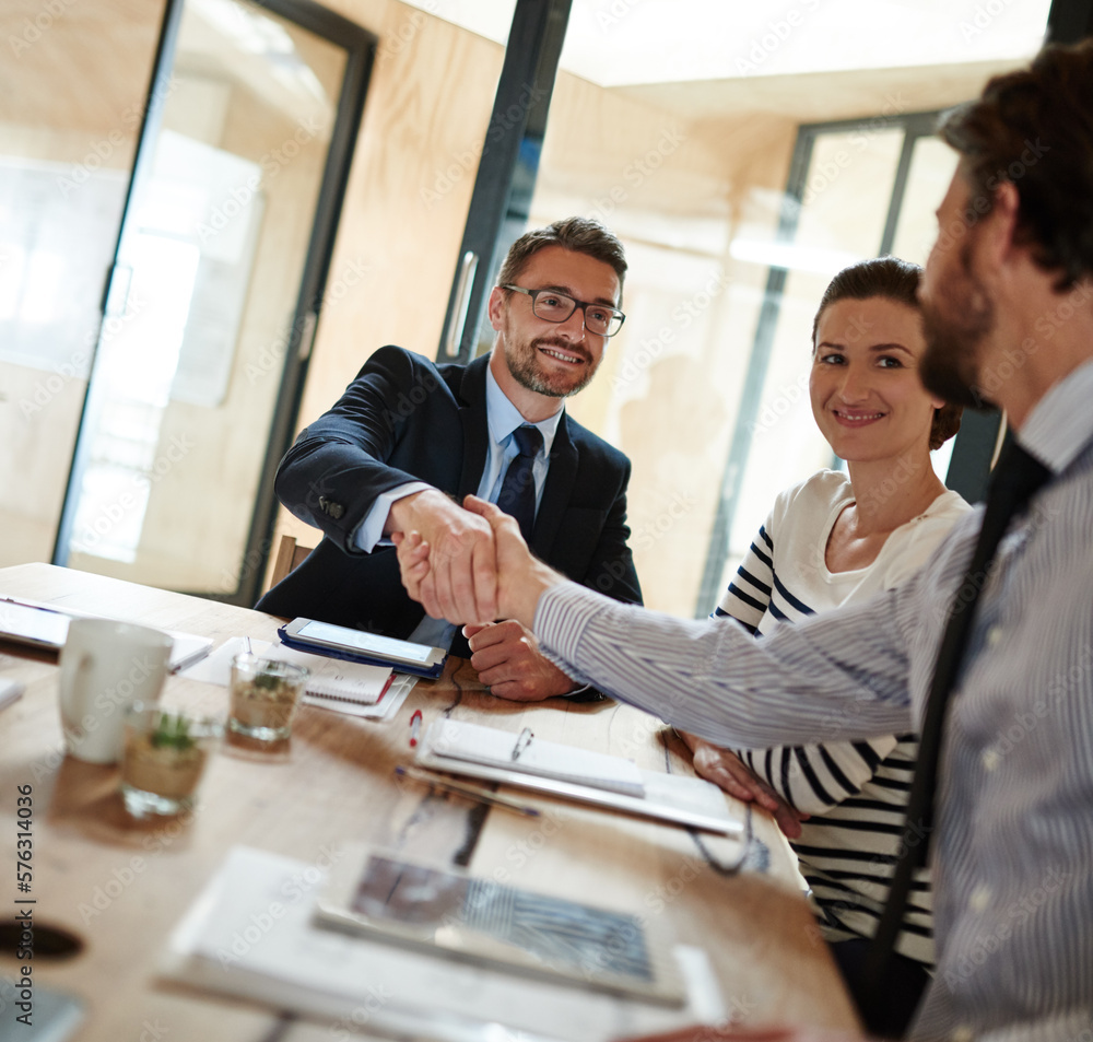 Poster making deals in the boardroom. shot of two businesspeople shaking hands in an office while a colleag
