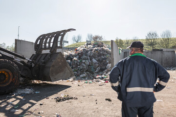 Recycling center worker, in dark blue work clothes, looking at an unsorted garbage heap just...