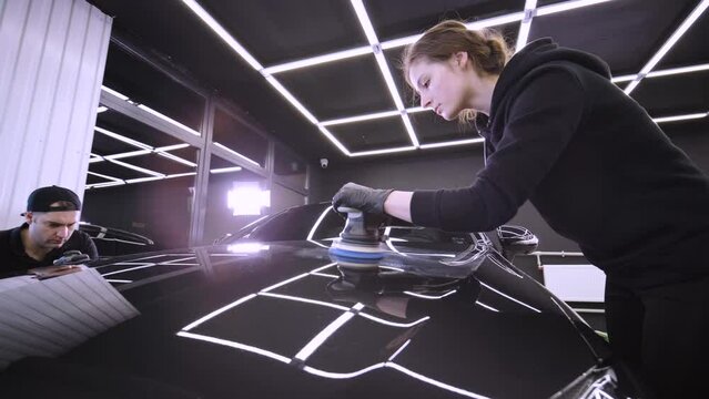 Worker polish a black car. Car detailing - woman are using machinery car polishers maintenance to remove marks repair according to the surface of the car's paint before contin