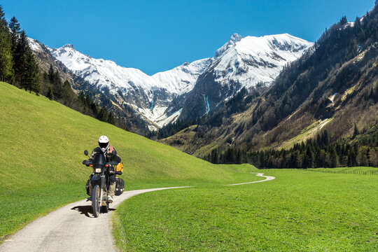One Motorbiker Man driving on mountain valley road with snow covered Mountains. Motorcycle Adventure in the Alps.