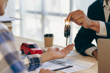 Car business, car sale, deal, gesture and concept of people close-up of dealer handing keys to new owners and shaking hands in showroom