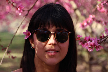 Face of young beautiful woman with pink flowers peach tree in her hair.