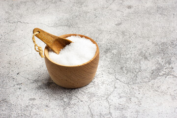 Sal dentro de un cuenco de madera junto a una cuchara sobre un fondo de mármol gris rústico y texturado. Vista de frente y de cerca. Copy space