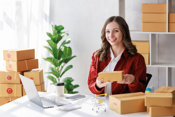 Concept of parcel delivery and selling online, seller or retailer smiling while holding a parcel box containing goods for preparing to deliver to the customer who ordered from her online store.