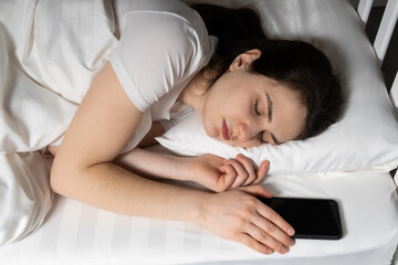 A 30-year-old woman sleeps with her phone near a pillow. Phone addict, online always