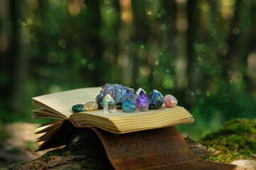 witch spell book and minerals on natural blurred forest background. Gemstones for healing Magic...