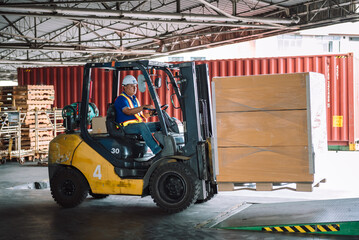 Asian male warehouse worker driving forklift for loading pallets in warehouse to container.