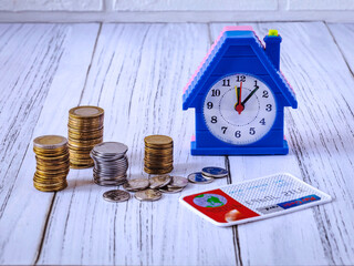 Money for real estate, home loan concept. Coins, credit card, alarm clock in the form of a house on a white wooden background