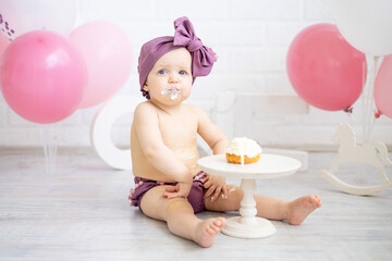 Fototapeta na wymiar a baby girl celebrates her first year on her birthday with pink balloons and eats her cake with her hands, smiles and rejoices