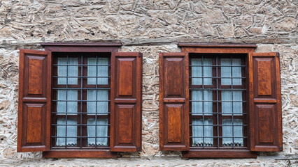 Fototapeta na wymiar Close-up wall of a stone house with wooden windows and shutters. Old european architecture