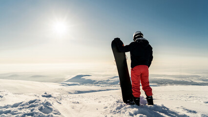 A male snowboarder in snowboarding gear at the top of a mountain, a view of the horizon peak....