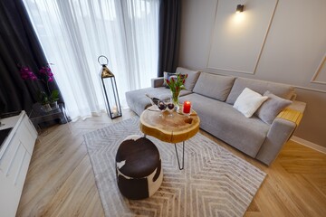 Przytulny apartament z wygidą sofą, na pierwszysm planie stolik kawowy z butelką wina i kieliszkami