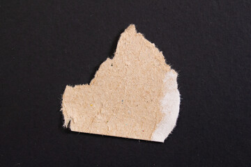 Ripped cardboard paper on black background. Torn paper piece.