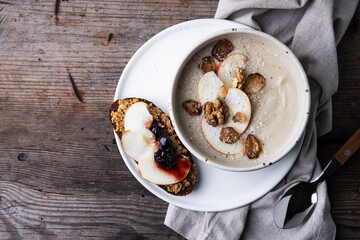 Bowl of homemade Jerusalem artichoke and apple cream soup and toast with homemade pate with fresh apple and cherry jam on wooden table.