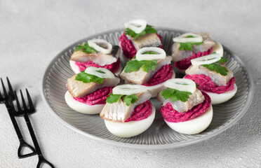Eggs stuffed with beets and salted herring, garnished with parsley and onion on gray background