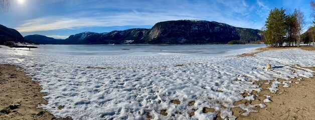 Panorama of Frozen Lake in Bygland, Norway, February 2023. Mountains behind with snow and blue skies. 