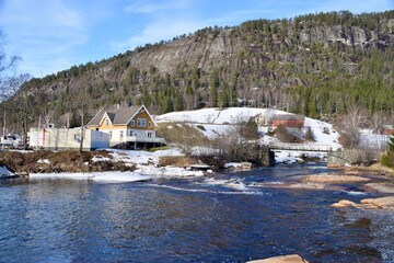 Bygland, Norway. February 21, 2023. River with houses and mountains behind. Snow on the ground. 