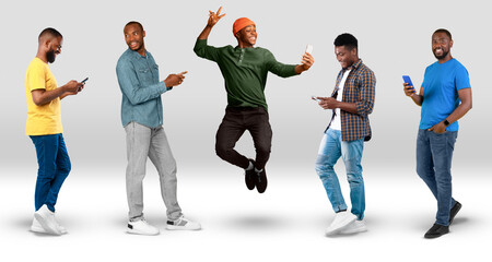 Smiling young black guys in casual typing on smartphones jumping, take selfie on white background