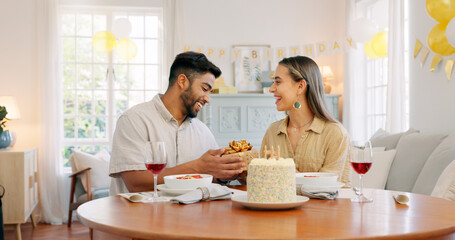 Interracial, couple and celebrate for birthday with gift, being happy and relax together at party. Romance, man and woman with present, bonding and smile in home in living room for hug and embrace.