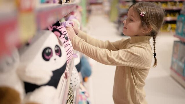 The girl is standing in a children's toy store in front the shelf and take a soft toy