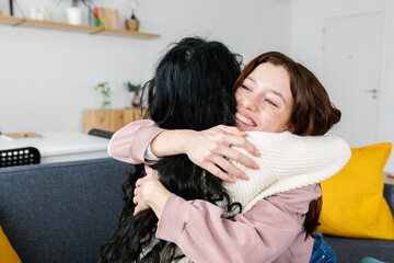 Smiling young teenage girl embracing her female friend showing affection on sofa at home. Human relationship, care and emotion concept