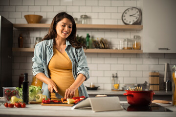 Young woman cutting vegetables in kitchen. Beautiful pregnant woman making salad.