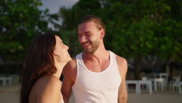 Young biracial happy couple holding hands and walking on the beach together enjoying summer closeup. Cheerful boyfriend and girlfriend relax and walk at the seaside hugging and kissing at sunrise.