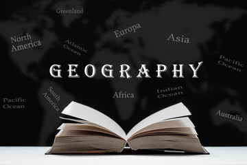 The study of geography. An open book, a textbook lies on the table. Map with names of continents and oceans on a black blurred background.