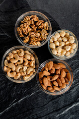 Assortment of nuts in glass bowls on a dark stone table. Cashews, hazelnuts, walnuts, almonds