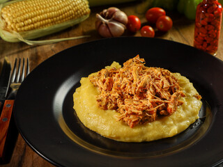 chicken with creamed corn (polenta) on a black plate with vegetables in the background