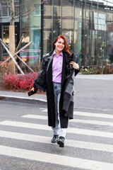 Attractive smiling business woman in casual clothing is walking in a city.