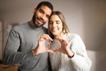 Happy young arab male hugging european woman show keys, make heart sign with hands in living room