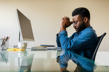 Upset pensive black businessman sitting at desk with computer, male professional analyst thinking of problem solution