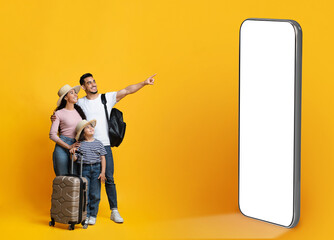 Happy parents with little daughter carrying suitcases, pointing at phone