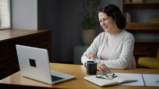 Happy woman smiling and waving hand, sitting in home and talking on video call using laptop camera. Online meeting with professional psychologist, freelance work, communication with beloved relatives.