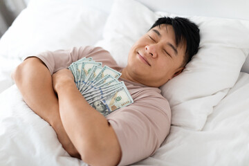 Happy sleeping chinese man hugging bunch of cash