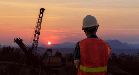 Rear view of a male engineer wearing a white helmet at a job site at dusk