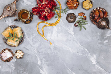 Stylish banner with traditional Arabic tableware and food sets, cup of tea, Koran and rosary on gray stone background. Ramadan table top view