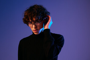 Male fashion portrait in black clothes model poses in close-up glasses, curly hair, hipster lifestyle, portrait blue background, mixed neon light, fashion style and trends boys teenager, copy space