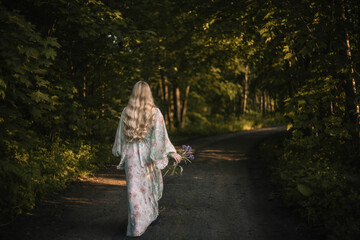 blonde woman with long hair in a dress walks through the forest, the concept of the beginning of summer.
