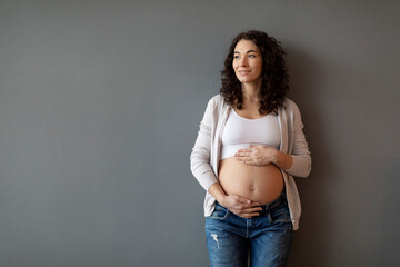 Beautiful young pregnant lady embracing her big belly and looking away