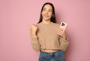 Portrait of a smiling casual woman holding smartphone over pink background