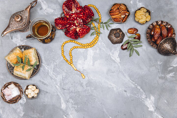 Stylish banner with traditional Arabic tableware and food sets, cup of tea, Koran and rosary on gray stone background. Ramadan table top view