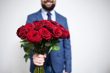 Man no face in a blue suit holding a luxurious bouquet of red roses on a grey background, mockup, place for text,copy space. Concept: holiday, valentines, relationships and mothers day, womens day.